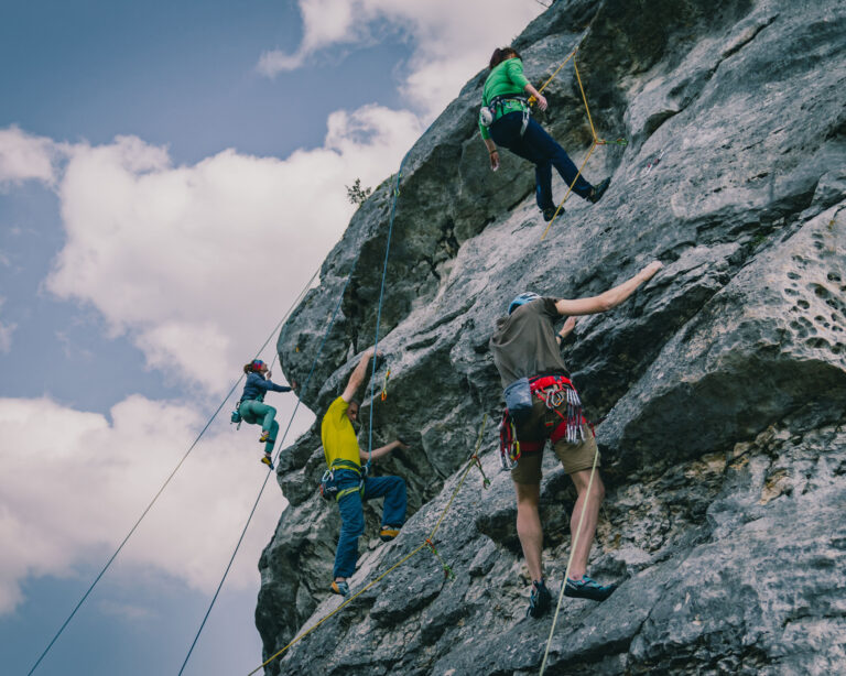 Low-angle rear of a people climbing a high rock, cloudy nd sunlit sky background