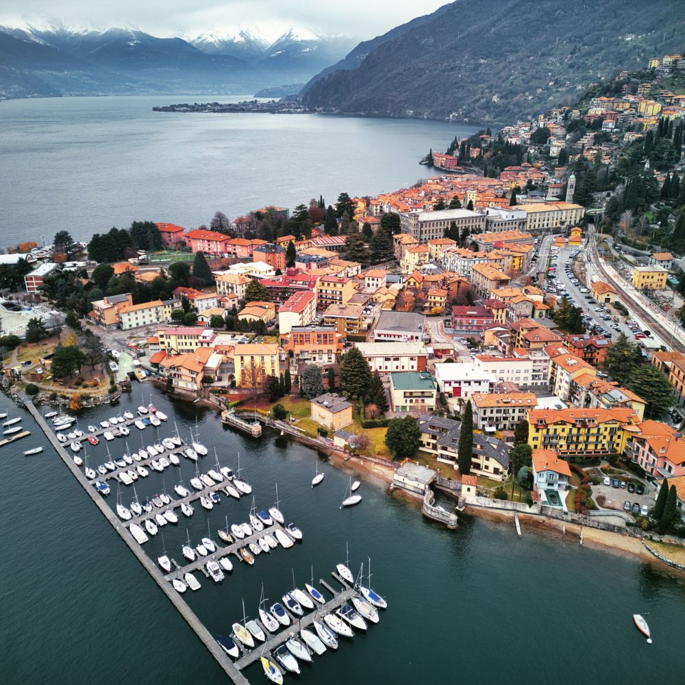 A drone view of Lake Como surrounded by a town and mountains in the evening in Italy