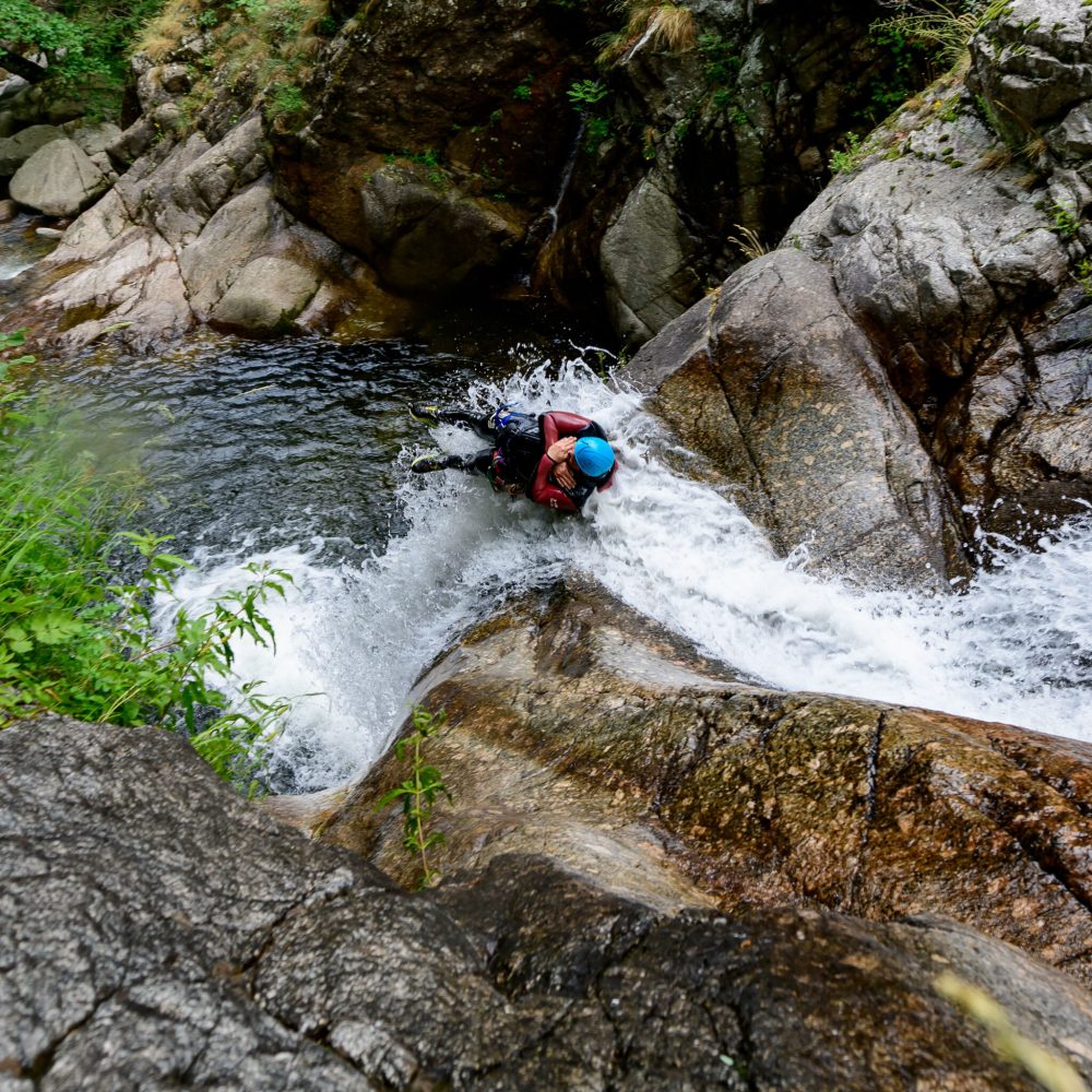 A high angle shot of people canyoning through a stream on the side of a mountain in France