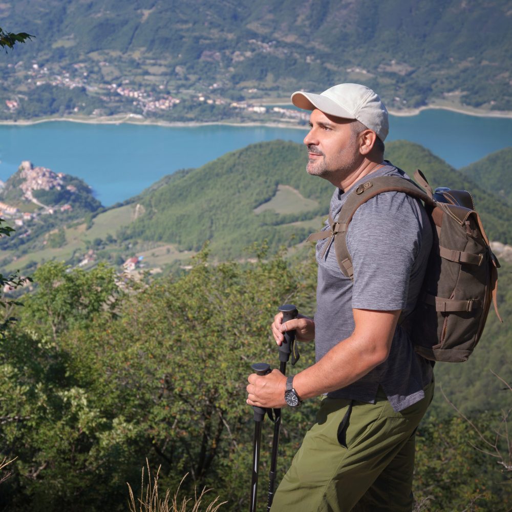 Man explorer in the mountains observes the landscape on the horizon, in the background a beautiful lake