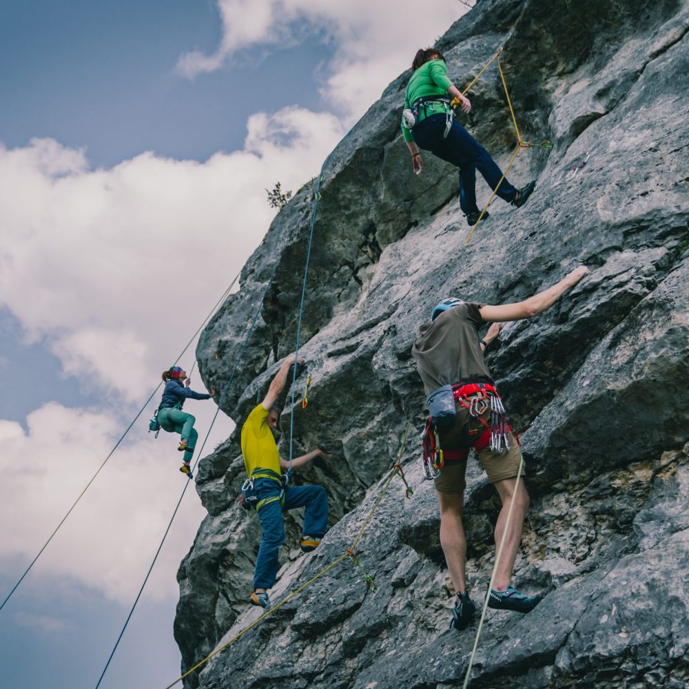 A low-angle rear of a people climbing a high rock, cloudy nd sunlit sky background