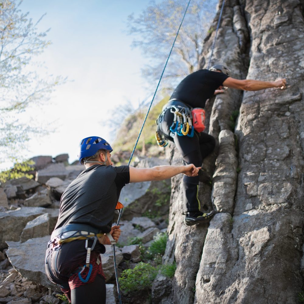 Portrait of senior man with instructor climbing rocks outdoors in nature, active lifestyle.