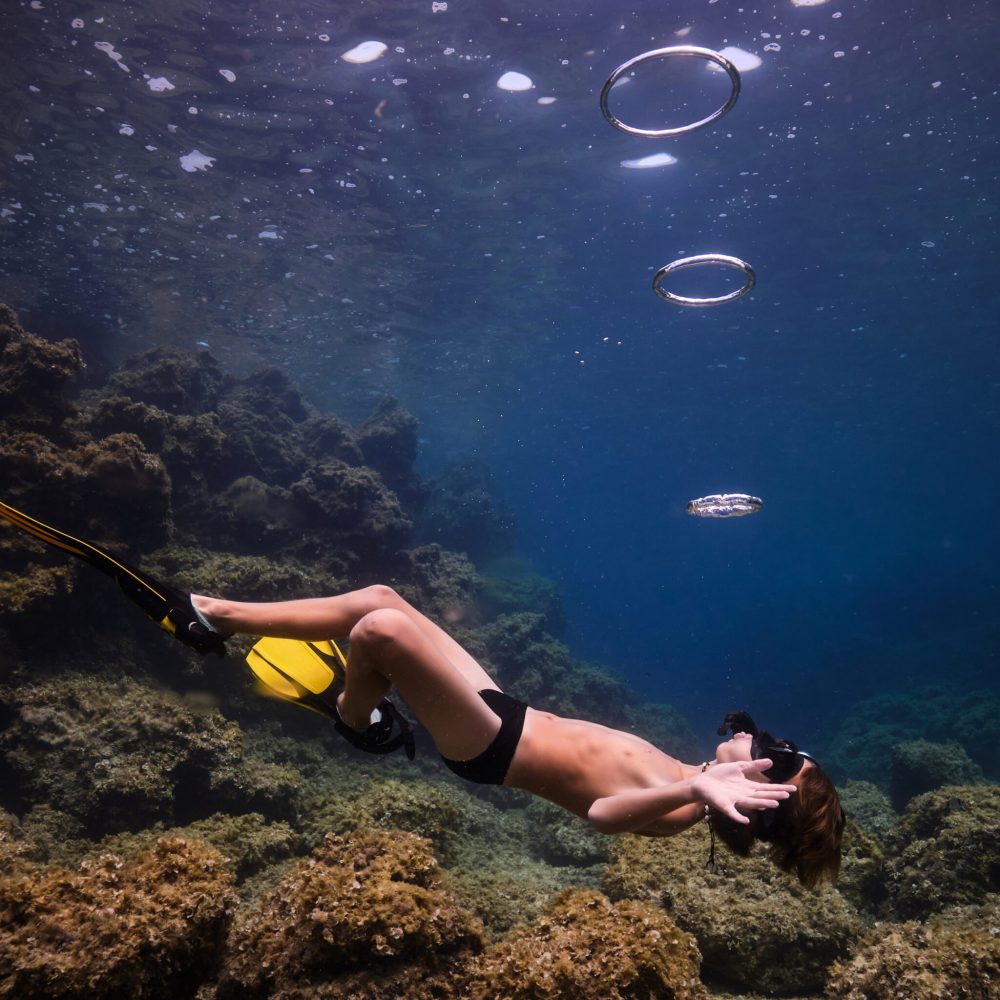 Side view full body of anonymous young shirtless man in snorkeling mask and flippers swimming under clear water of ocean near coral reefs in daylight